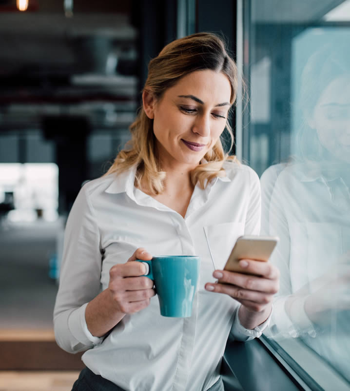 woman holding phone with hot drink